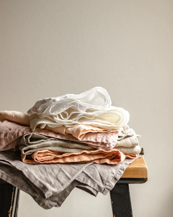 A stack of folded linen cloths in warm and neutral tones on a stool