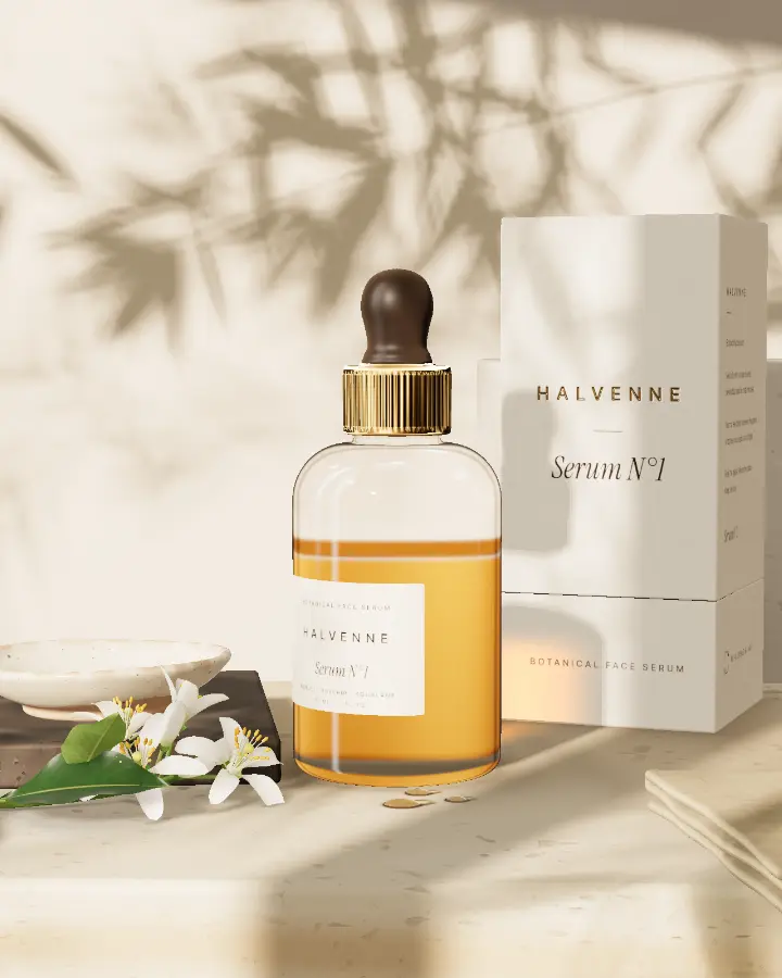 Serum N°1: a clear glass bottle with a brass collar and a dark dropper bulb, beside its carton, orange blossom and a stone dish in morning sun