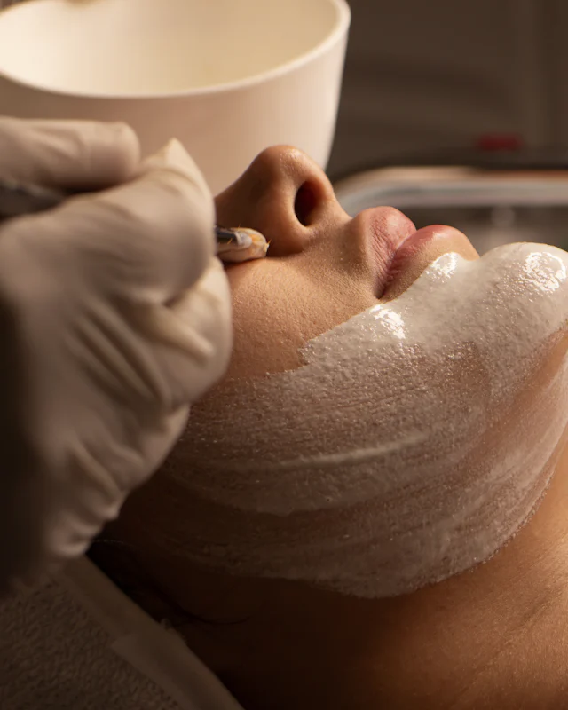 Gloved hands smoothing a white mask over the jaw and lips during a facial