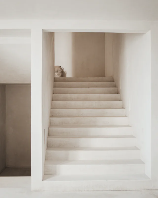 A plain plaster stair rising between pale limewashed walls to a landing
