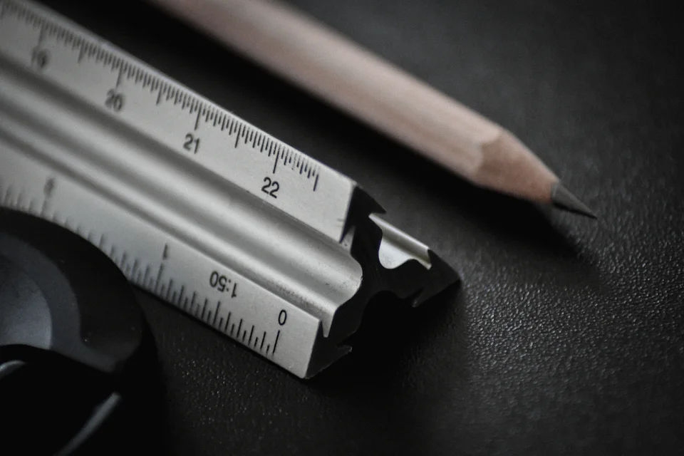 The end of an aluminium scale ruler and a sharpened pencil on a dark desk
