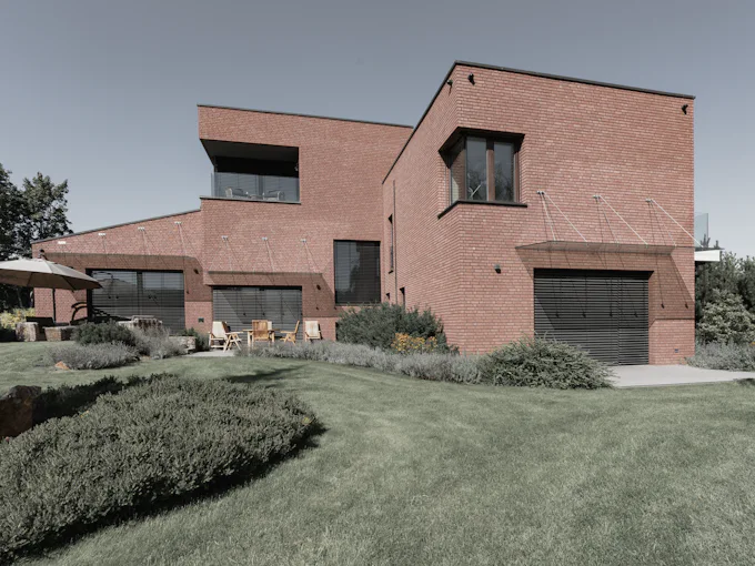 A modern red-brick family house of stacked volumes with deep-set windows, above a sloping lawn