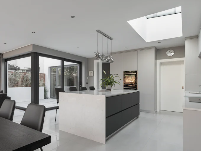 A kitchen in a rear extension: a stone-topped island under a roof light, and black-framed glazing to a small terrace
