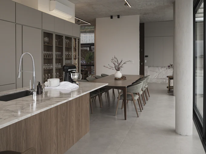 An open kitchen with a long oak-fronted island running into a dining table, under a concrete ceiling