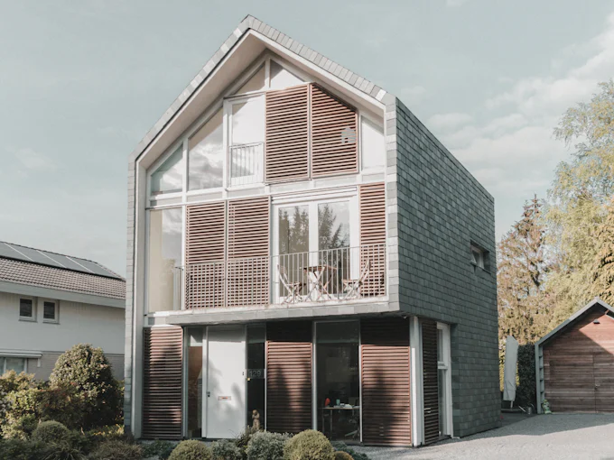 A new family house with a glazed gable behind timber louvres and dark slate-clad sides