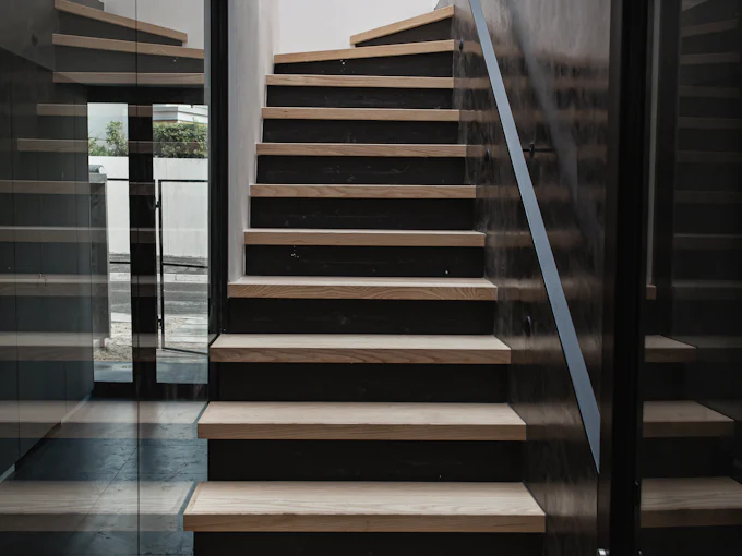 An oak stair with open treads between a dark wall and a glass screen