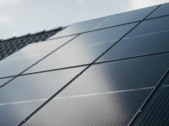All-black solar panels in rows over a tiled roof, against a pale sky