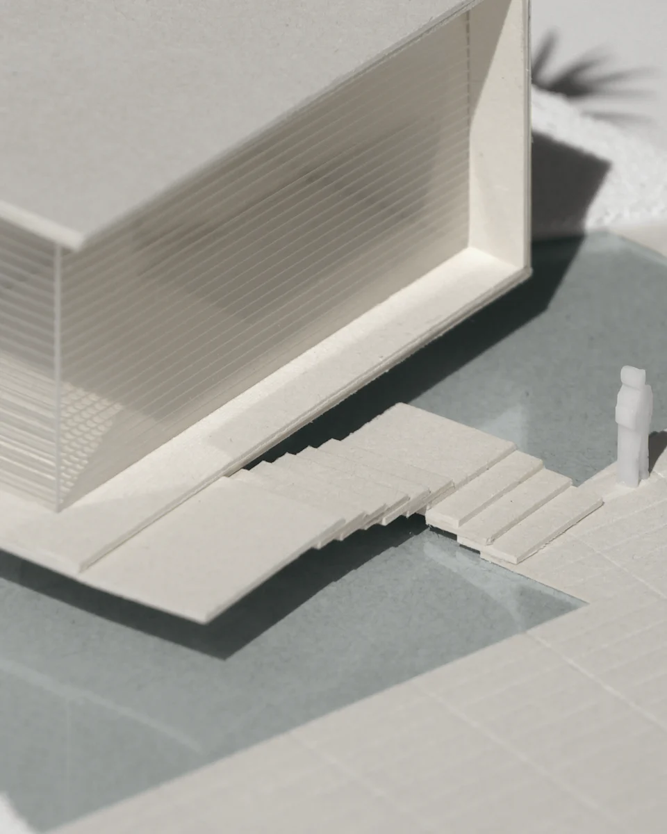 A white study model of a house, with a stair down to a terrace and one tiny scale figure