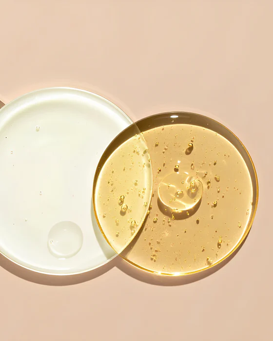 Three glass discs of clear gel, white lotion and golden serum, one with a small green leaf, on a pale peach surface