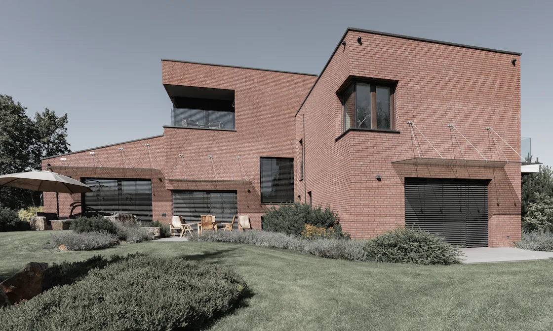 A modern red-brick family house of stacked volumes with deep-set windows, above a sloping lawn