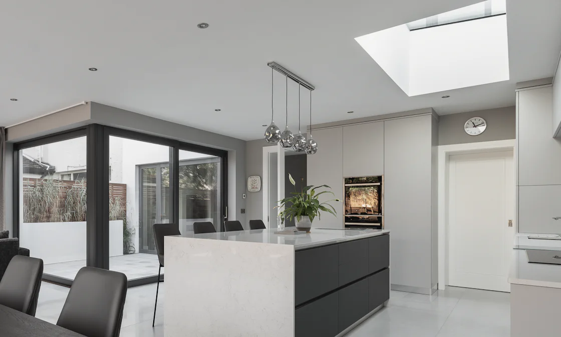 A kitchen in a rear extension: a stone-topped island under a roof light, and black-framed glazing to a small terrace