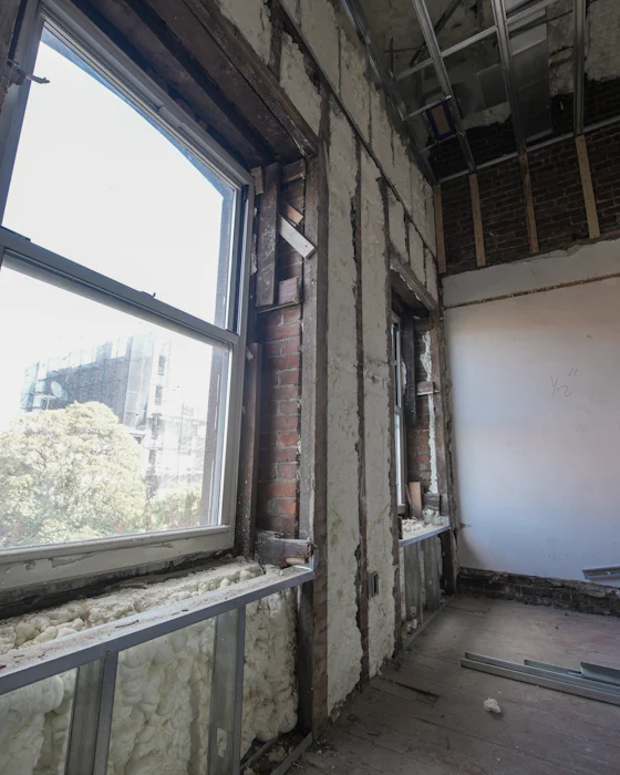 A room during renovation: insulation between metal studs against old brick walls, beside a tall window