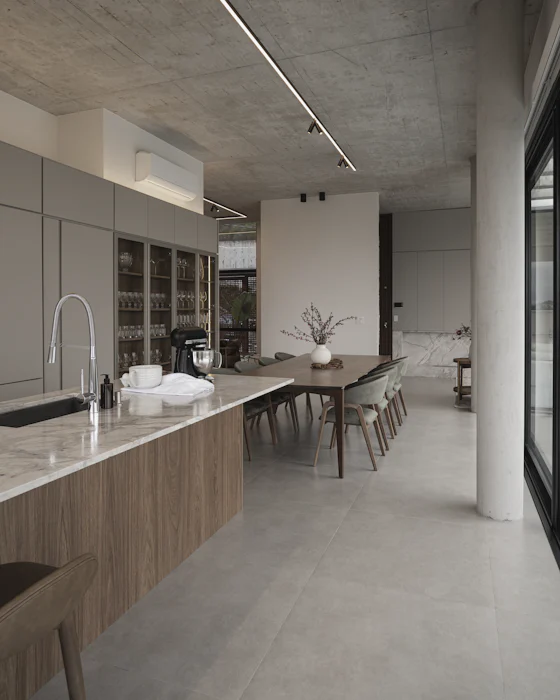 An open kitchen with a long oak-fronted island running into a dining table, under a concrete ceiling