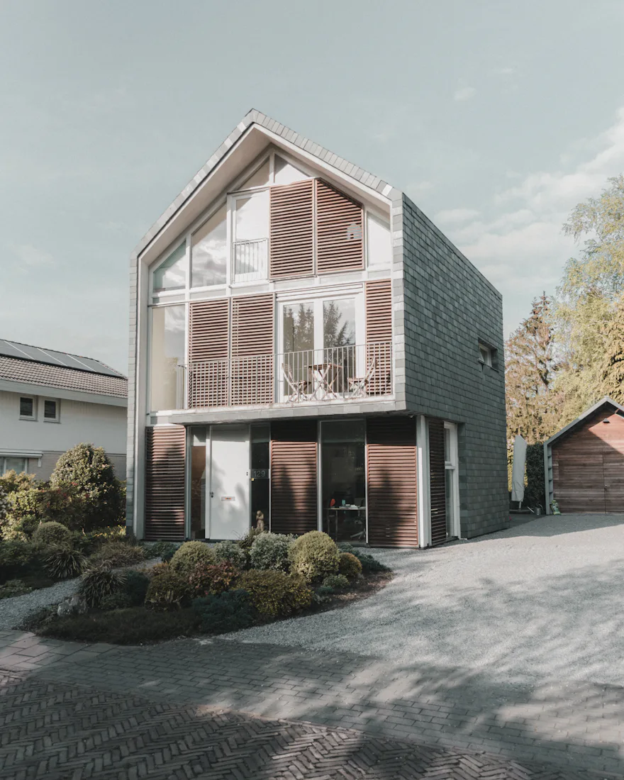 A new family house with a glazed gable behind timber louvres and dark slate-clad sides