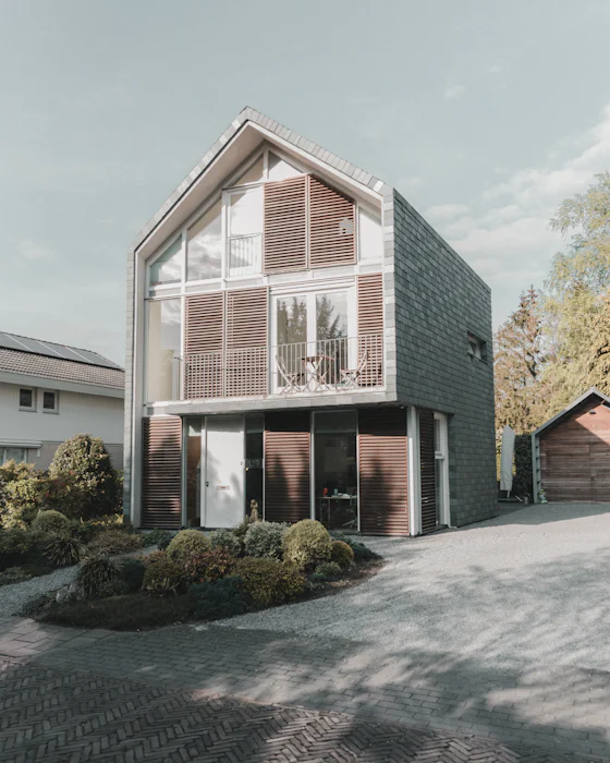 A new family house with a glazed gable behind timber louvres and dark slate-clad sides