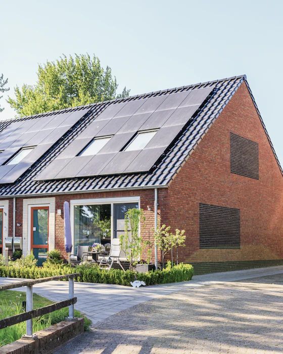 A row of red-brick terraced houses with black solar panels covering the roofs, under a clear sky