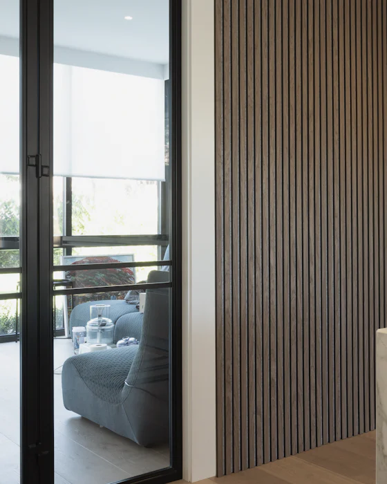 A black steel-framed glass door beside a wall of vertical wooden slats, a living room beyond it