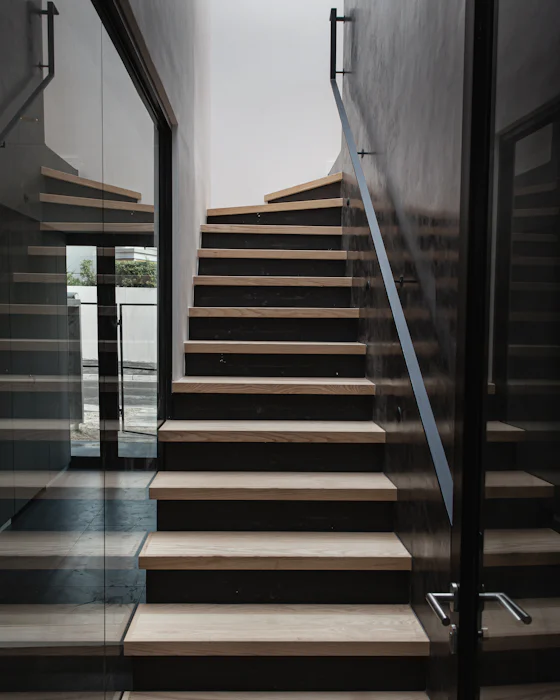 An oak stair with open treads between a dark wall and a glass screen