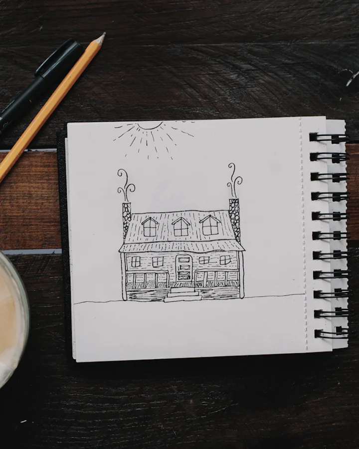 A small pencil drawing of a house in a notebook, next to a cup of coffee