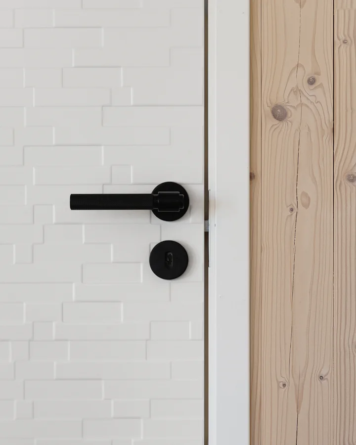 A black lever handle on a white door with a raised brick pattern, pale timber boards beside it