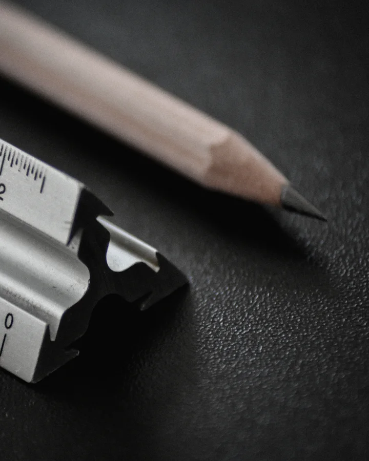 The end of an aluminium scale ruler and a sharpened pencil on a dark desk