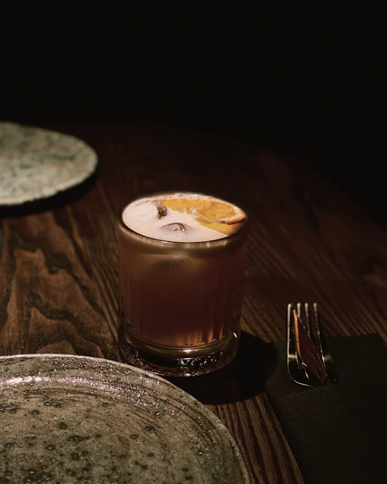 A cocktail with a slice of dried orange on a dark wooden table