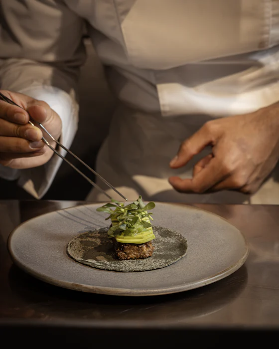 A cook placing herbs with tweezers at the pass