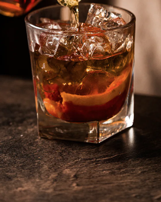 An amber spirit poured over ice and orange peel in a tumbler