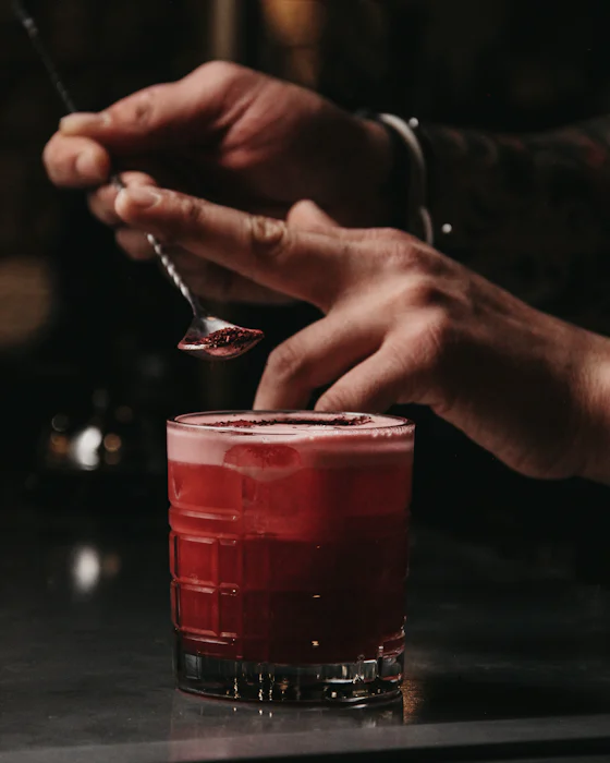 A red cocktail and a bar spoon on a dark bar