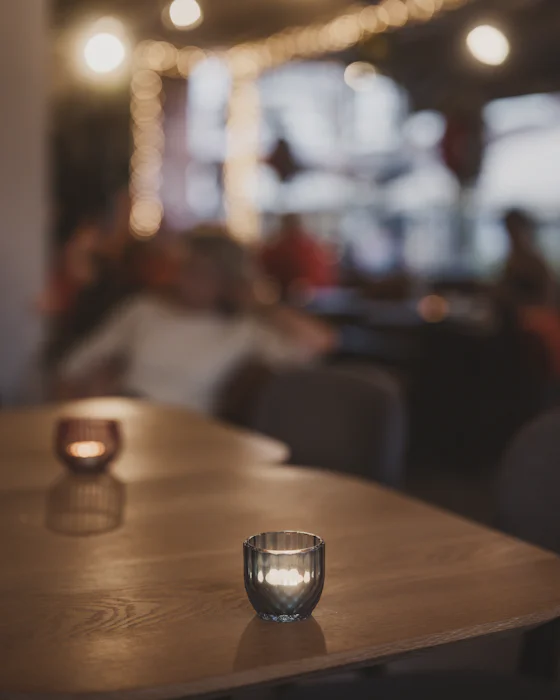 Two candles in glass holders on a wooden table, the room soft behind