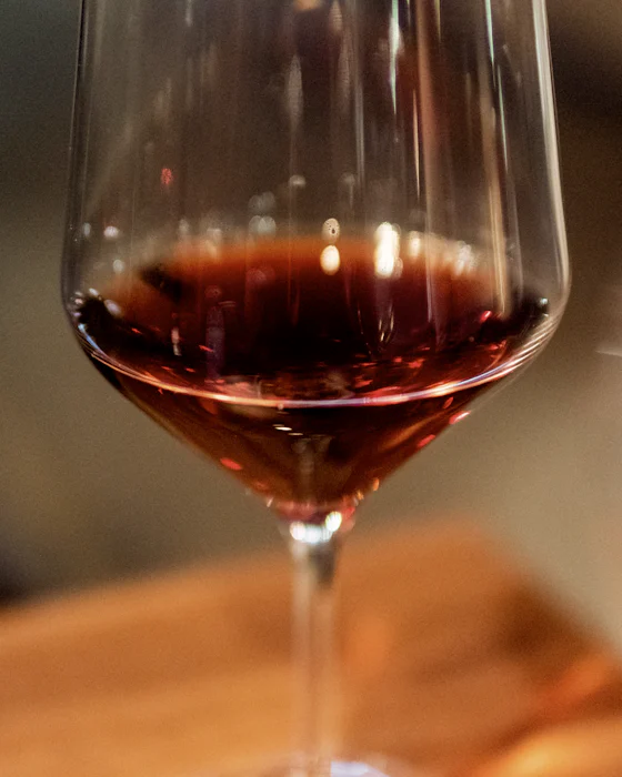 A glass of red wine on a wooden table, the room blurred behind it