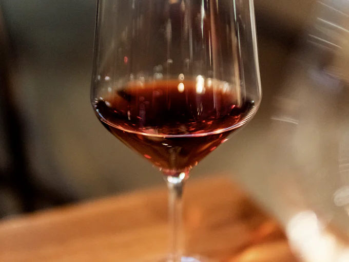 A glass of red wine on a wooden table, the room blurred behind it