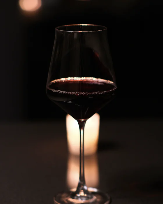 A glass of red wine, a candle glowing behind it